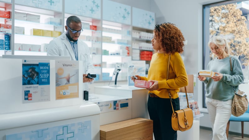 Two people waiting in line to purchase prescriptions at the pharmacy counter. 